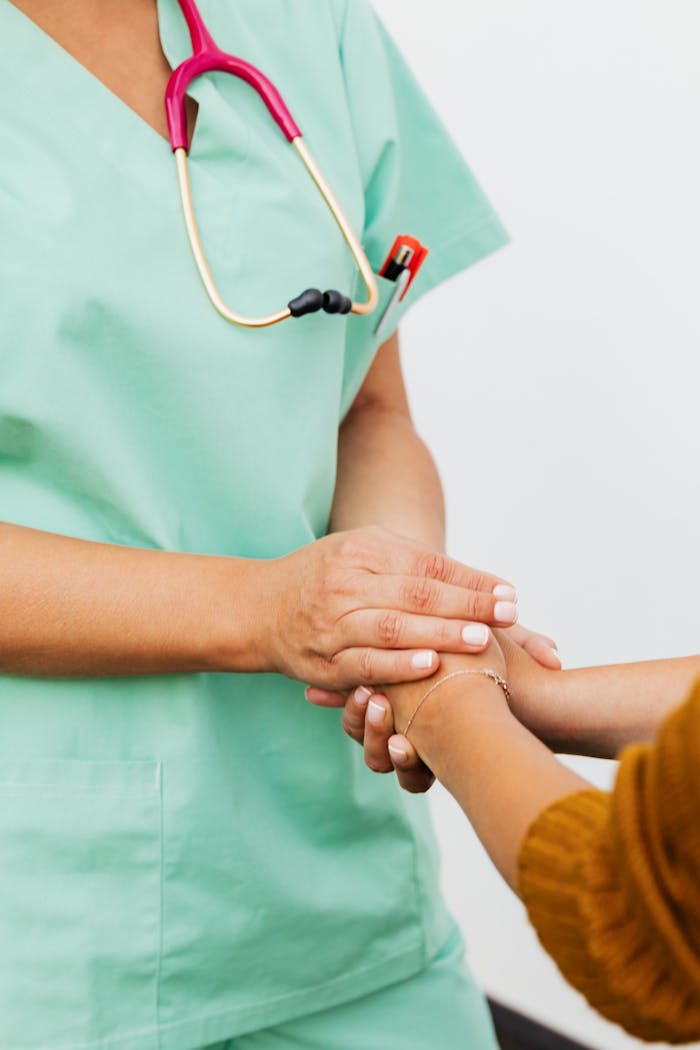 A nurse in green scrubs gently clasps a patient